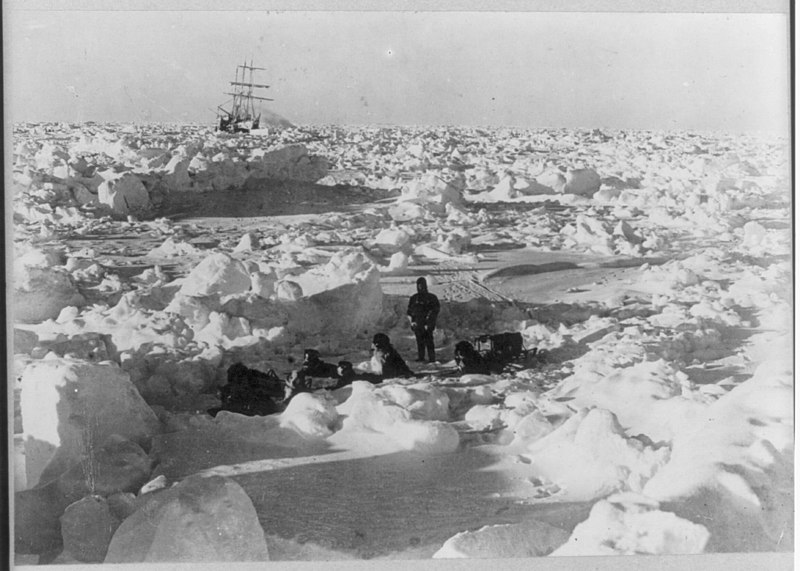 De bemanning in een kamp op het ijs, met in de verte de vastgevroren Endurance