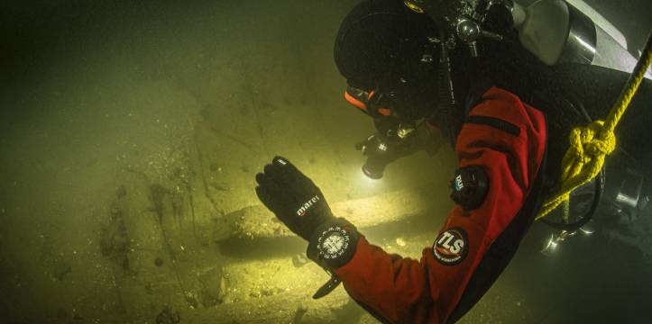 Een duiker schijnt met een zaklamp op de gezonken boot uit de 17e eeuw.