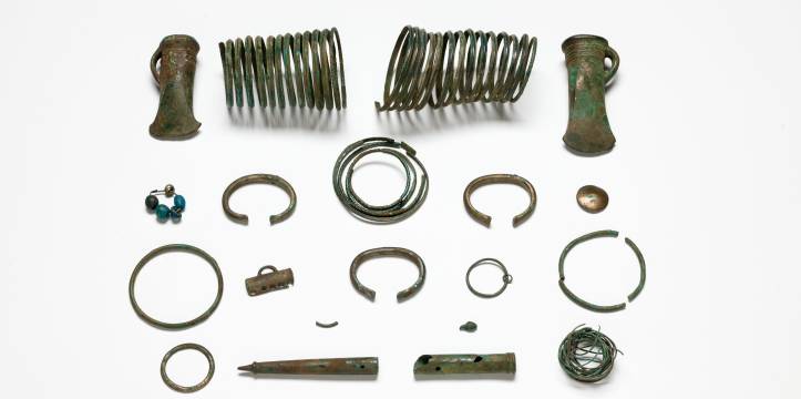 Onder de bronzen voorwerpen zijn twee spiraalarmbanden, twee kokerbijlen, verschillende armbanden, een knoop voor op kleding, de boven- en onderkant van een (waarschijnlijk ceremoniële) staf en een bronzen koord met één bronzen kraal en vijf glazen kralen eraan