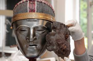 Het maskerfragment naast een replica van een Bataafs gezichtsmasker.